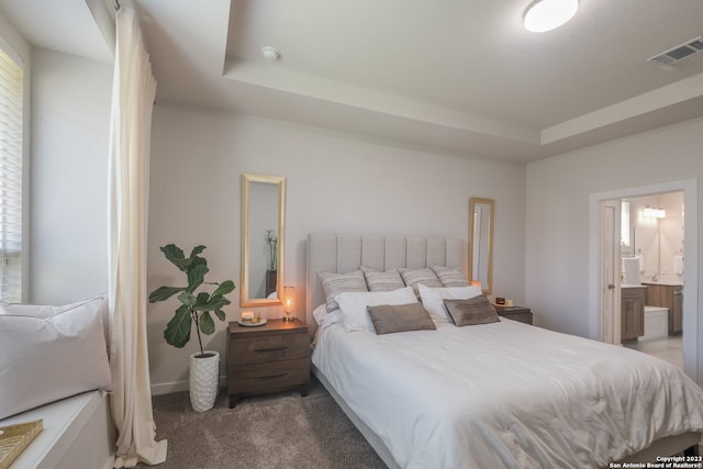 bedroom with a raised ceiling, connected bathroom, and dark colored carpet