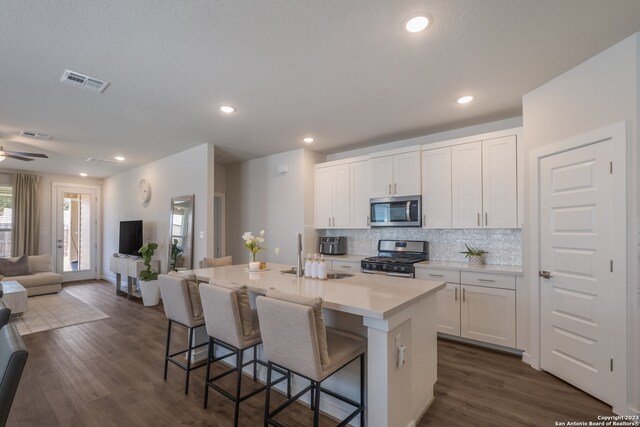 kitchen with ceiling fan, white cabinets, appliances with stainless steel finishes, a breakfast bar area, and a center island with sink