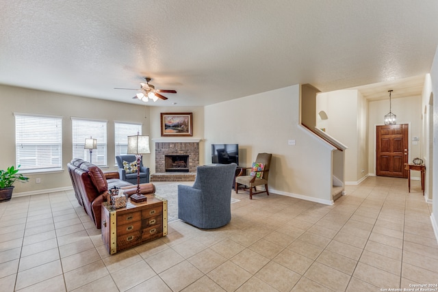 living room featuring light tile flooring, ceiling fan, a textured ceiling, and a fireplace