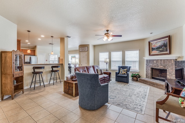 living room featuring light tile flooring, a textured ceiling, a fireplace, and ceiling fan