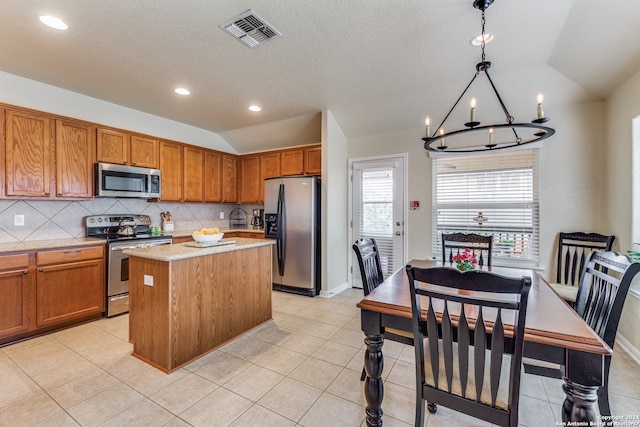 kitchen featuring appliances with stainless steel finishes, light tile flooring, a center island, a notable chandelier, and decorative light fixtures