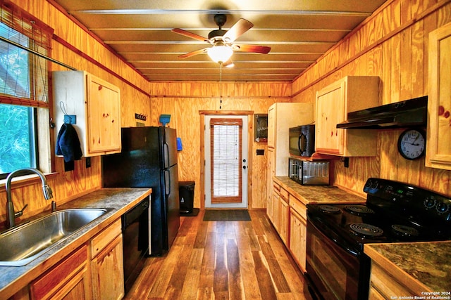 kitchen with ceiling fan, wooden walls, black appliances, sink, and wood-type flooring