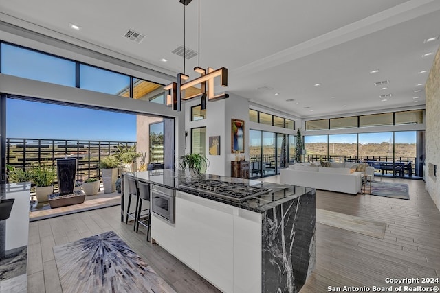 kitchen with stainless steel gas stovetop, light hardwood / wood-style flooring, dark stone countertops, a breakfast bar area, and pendant lighting