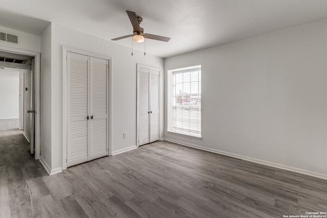 unfurnished bedroom featuring ceiling fan, dark wood-type flooring, and multiple closets