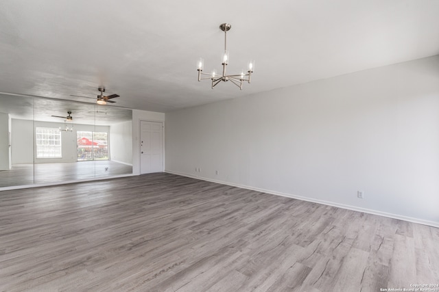 unfurnished living room with ceiling fan with notable chandelier and light hardwood / wood-style flooring