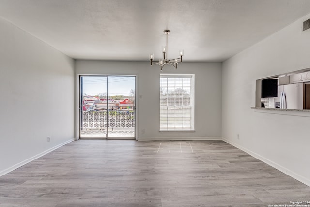 spare room with an inviting chandelier and light wood-type flooring