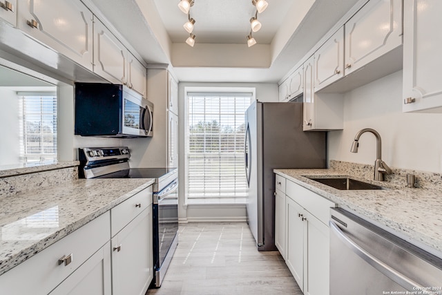 kitchen with sink, light stone counters, rail lighting, white cabinets, and stainless steel appliances