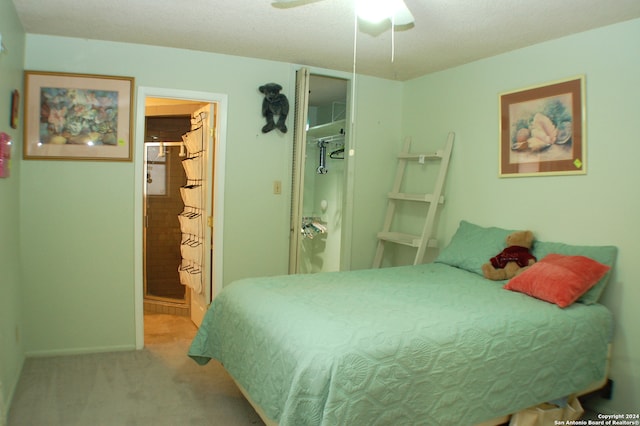 bedroom with ceiling fan, connected bathroom, light carpet, and a textured ceiling