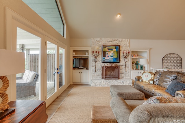 living room with built in shelves, lofted ceiling, light wood-type flooring, and a stone fireplace