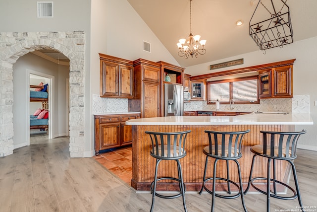 kitchen with an inviting chandelier, tasteful backsplash, pendant lighting, stainless steel fridge, and a kitchen breakfast bar