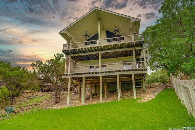 back house at dusk featuring a balcony and a lawn