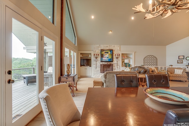 dining room with a notable chandelier, light wood-type flooring, a fireplace, and high vaulted ceiling