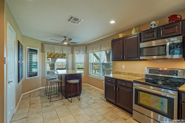 kitchen featuring ceiling fan, light tile patterned floors, appliances with stainless steel finishes, and a kitchen bar