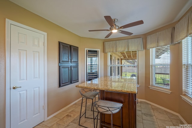 kitchen with ceiling fan, light tile patterned flooring, a kitchen bar, and light stone counters