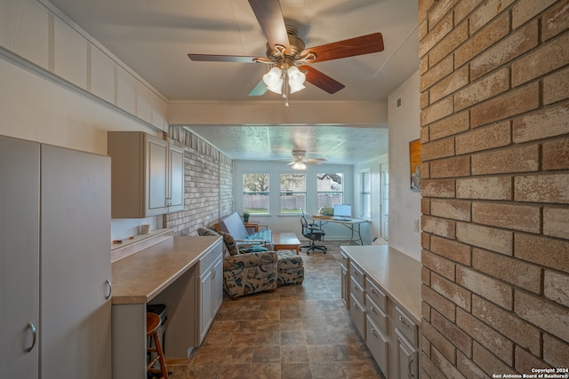 kitchen featuring ceiling fan, dark tile patterned floors, and brick wall