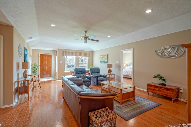 living room featuring lofted ceiling, light wood-type flooring, a textured ceiling, and ceiling fan