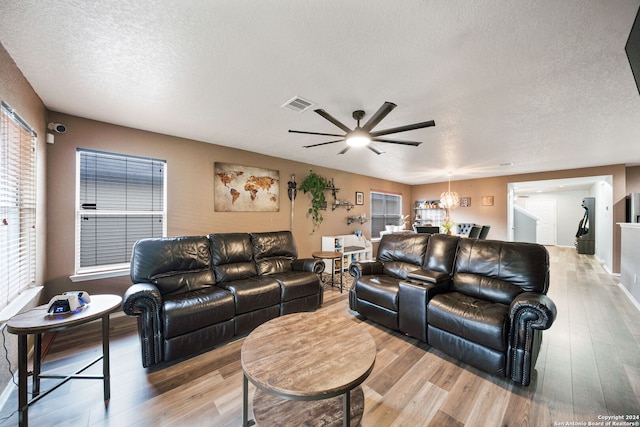 living room featuring a textured ceiling, ceiling fan with notable chandelier, and light hardwood / wood-style flooring