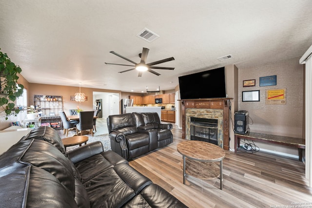 living room featuring a fireplace, light hardwood / wood-style floors, and ceiling fan with notable chandelier