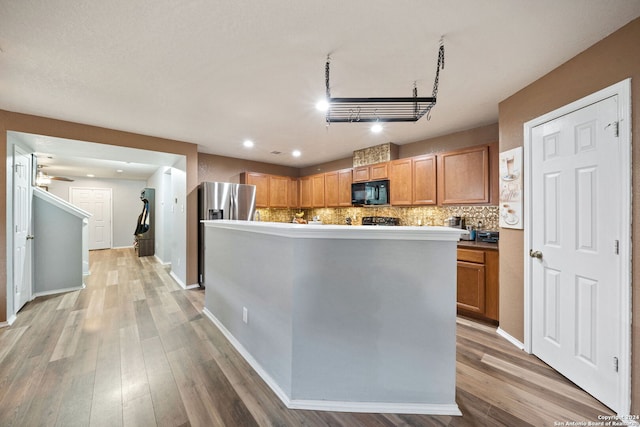 kitchen with a kitchen island, ceiling fan, tasteful backsplash, stainless steel fridge, and light wood-type flooring