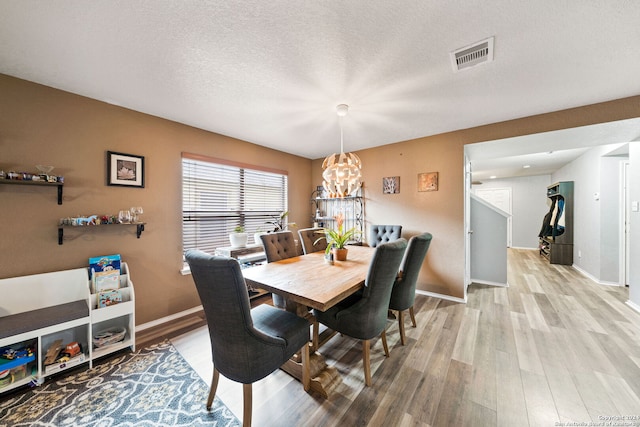 dining room with a textured ceiling, a chandelier, and light hardwood / wood-style floors