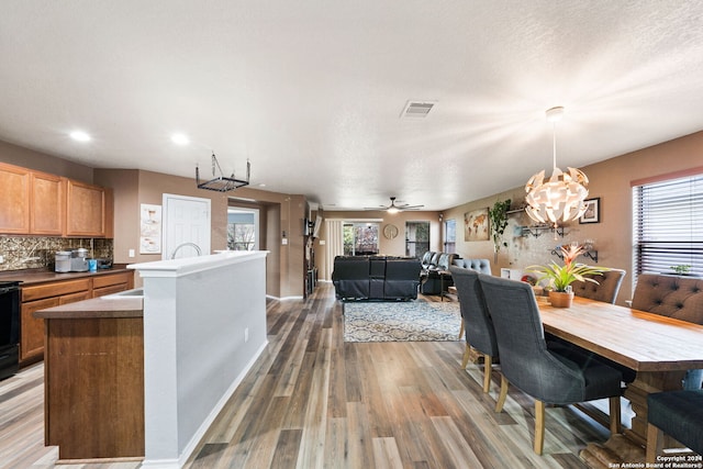 dining room with a textured ceiling, wood-type flooring, ceiling fan with notable chandelier, and a healthy amount of sunlight