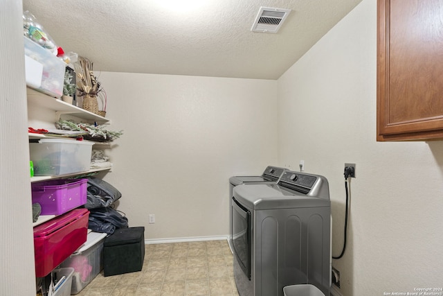 clothes washing area with light tile flooring, hookup for an electric dryer, a textured ceiling, cabinets, and washer and dryer