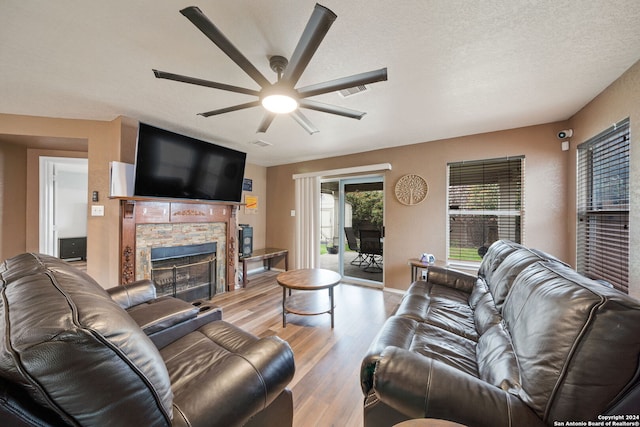 living room with light hardwood / wood-style floors, ceiling fan, a textured ceiling, and a fireplace