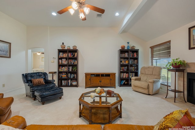 carpeted living room featuring a tile fireplace, lofted ceiling with beams, and ceiling fan