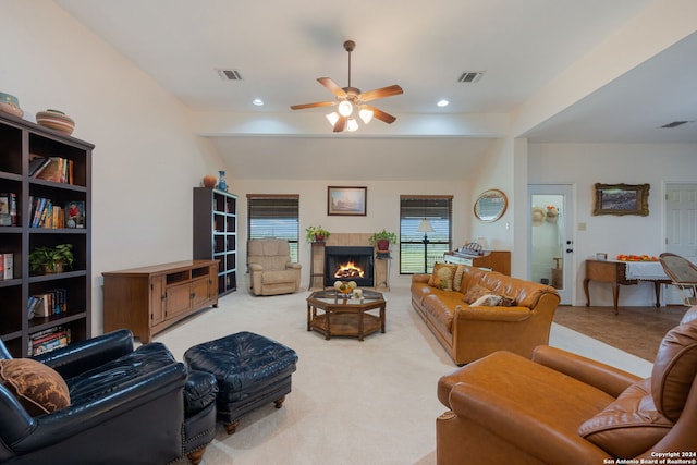 living room with light colored carpet, vaulted ceiling, ceiling fan, and a tiled fireplace