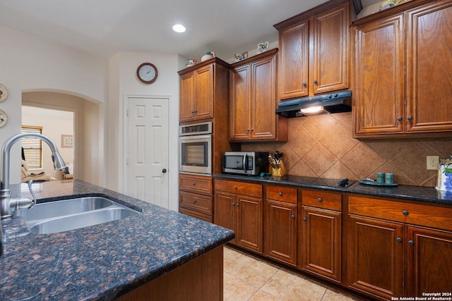 kitchen featuring sink, stainless steel appliances, dark stone countertops, decorative backsplash, and light tile patterned flooring