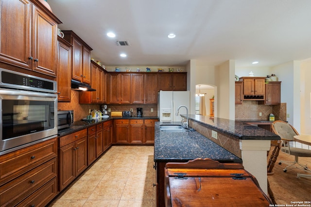 kitchen featuring tasteful backsplash, dark stone counters, a breakfast bar, stainless steel appliances, and sink