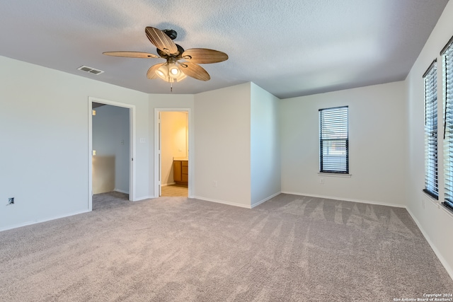 unfurnished bedroom with light carpet, ensuite bath, ceiling fan, and multiple windows