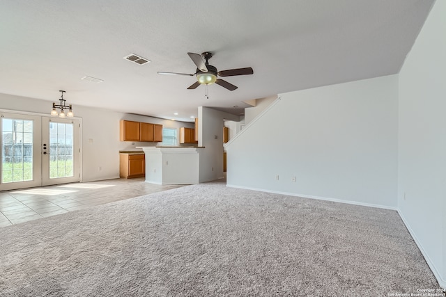 unfurnished living room with light colored carpet, french doors, and ceiling fan with notable chandelier