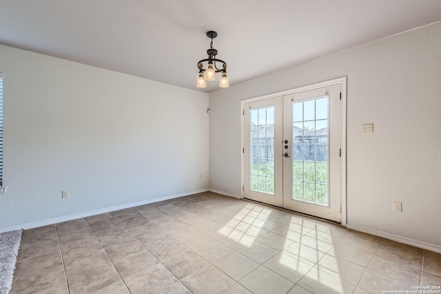 tiled spare room featuring french doors, a healthy amount of sunlight, and a chandelier