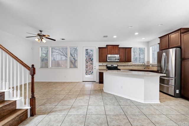 kitchen with ceiling fan, light tile floors, backsplash, stainless steel appliances, and a center island