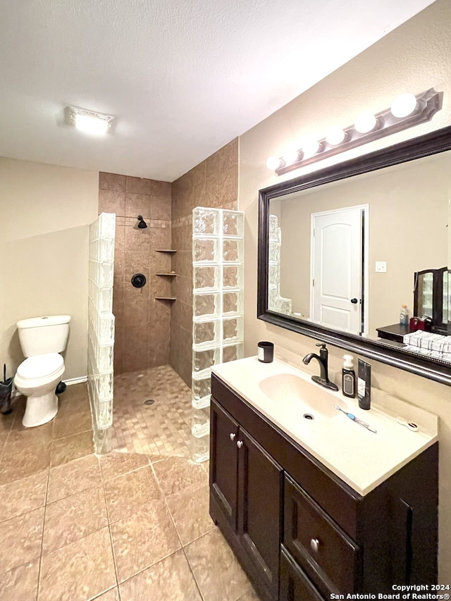 bathroom with tile floors, a textured ceiling, toilet, vanity, and a tile shower