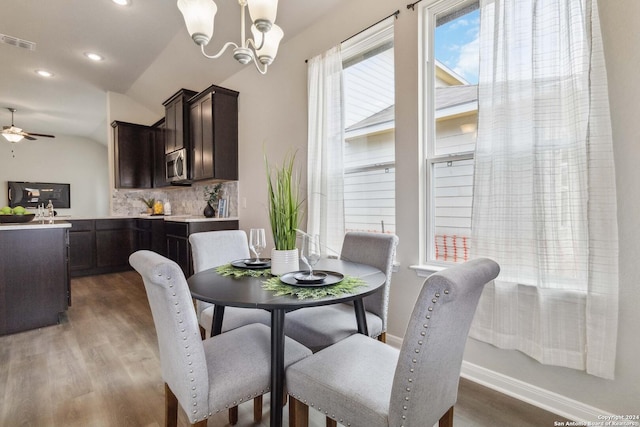 dining room with a healthy amount of sunlight, ceiling fan with notable chandelier, dark hardwood / wood-style floors, and vaulted ceiling