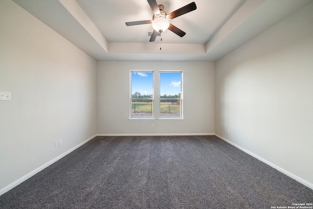 empty room with a raised ceiling, ceiling fan, and dark carpet