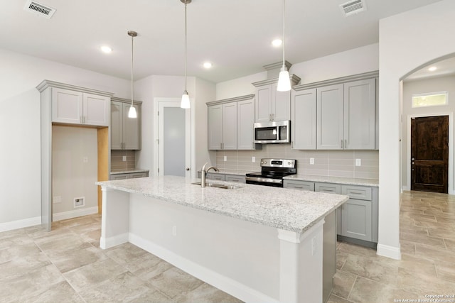 kitchen featuring pendant lighting, stainless steel appliances, backsplash, a kitchen island with sink, and light stone counters