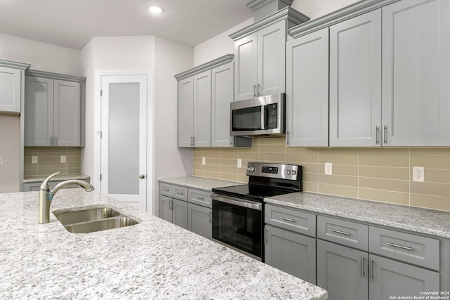 kitchen with backsplash, stainless steel appliances, sink, and light stone countertops