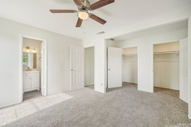 unfurnished bedroom with light carpet, sink, ensuite bathroom, ceiling fan, and multiple closets