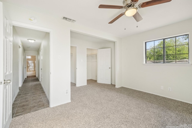 unfurnished bedroom featuring a closet, a walk in closet, ceiling fan, and carpet floors