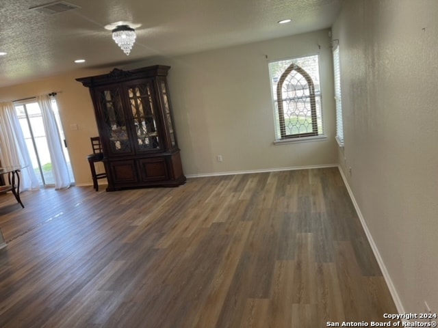 unfurnished living room featuring a healthy amount of sunlight, a textured ceiling, a notable chandelier, and dark hardwood / wood-style floors