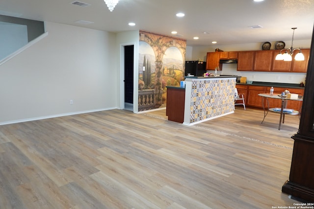 kitchen featuring decorative light fixtures, a notable chandelier, light hardwood / wood-style flooring, black fridge, and a kitchen island