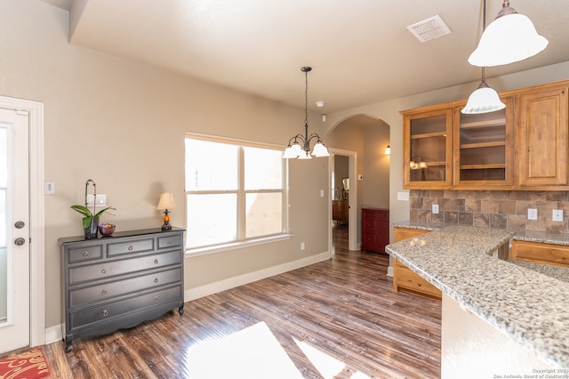 kitchen with dark wood-type flooring, light stone counters, hanging light fixtures, and decorative backsplash