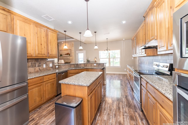 kitchen with appliances with stainless steel finishes, dark hardwood / wood-style floors, tasteful backsplash, and a kitchen island