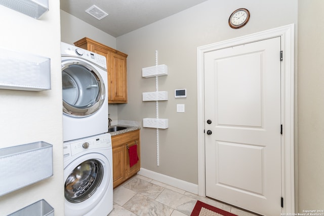 laundry room featuring light tile patterned flooring, stacked washer and clothes dryer, and cabinets