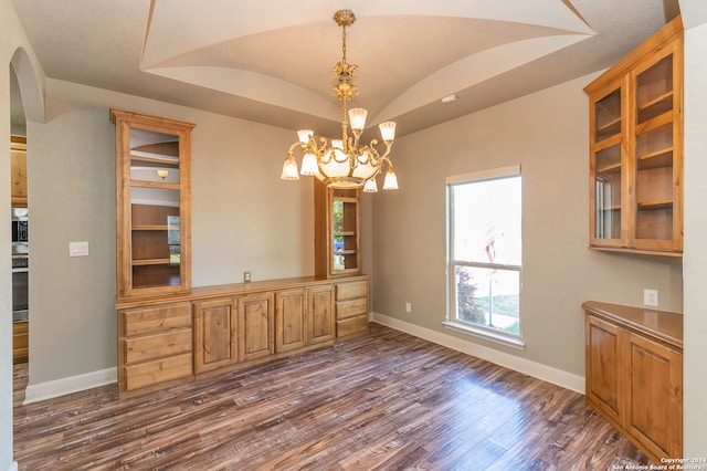 unfurnished dining area with dark hardwood / wood-style flooring, an inviting chandelier, and a raised ceiling