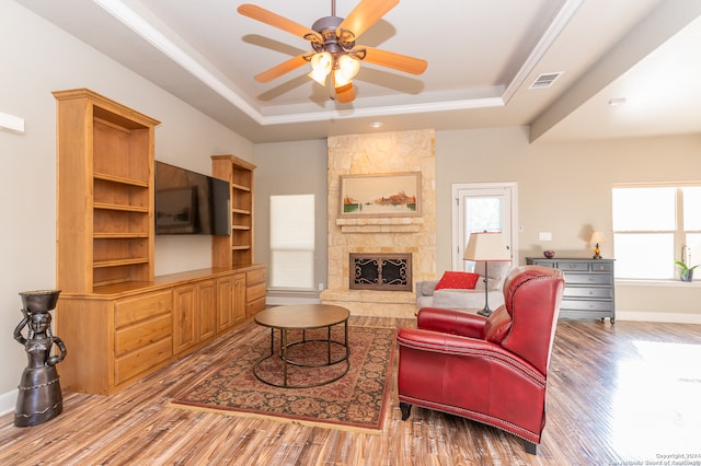 living room featuring ceiling fan, a stone fireplace, hardwood / wood-style flooring, and a raised ceiling