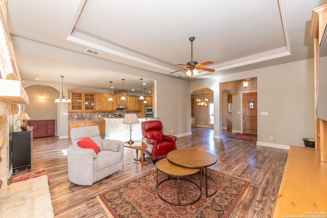 living room featuring light wood-type flooring, ceiling fan with notable chandelier, and a tray ceiling